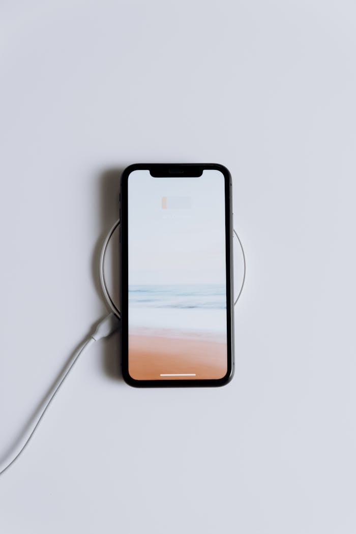 about-us Minimalist smartphone on a wireless charger with a serene beach wallpaper.